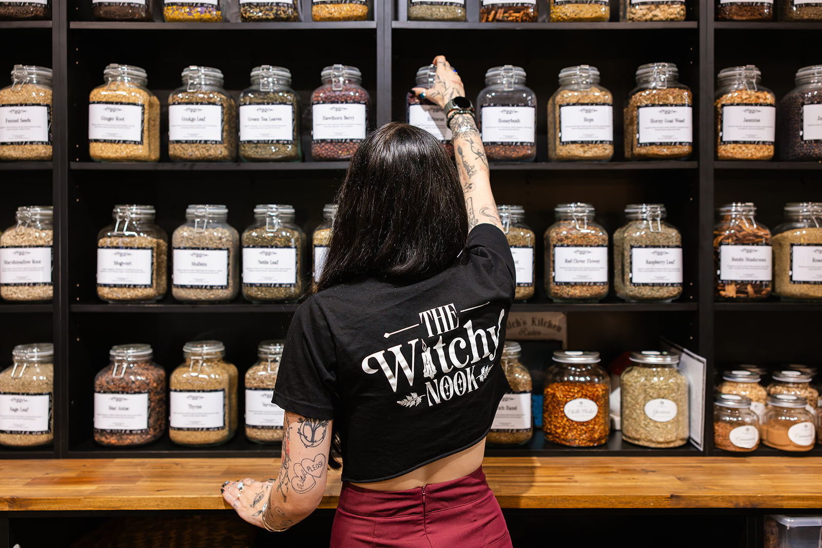 Owner of The Witchy Nook in the apothecary in front of a large selection of herbs in jars