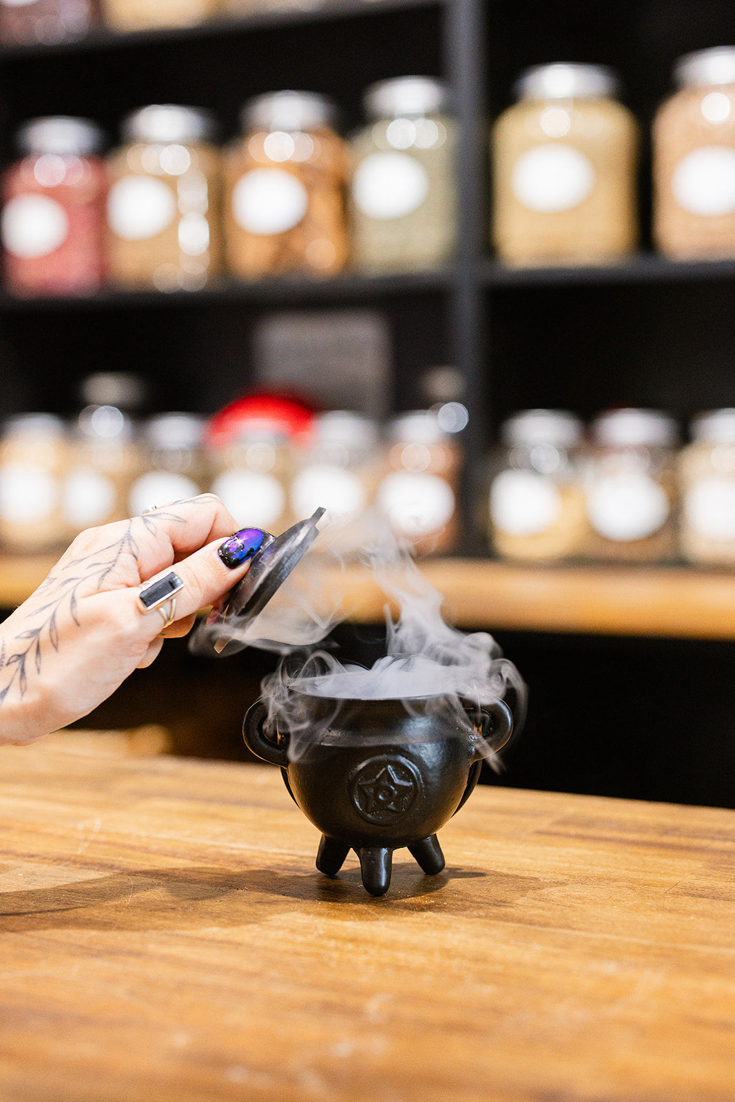 A woman's hand opening a small cauldron that has with smoke wisps escaping from inside 