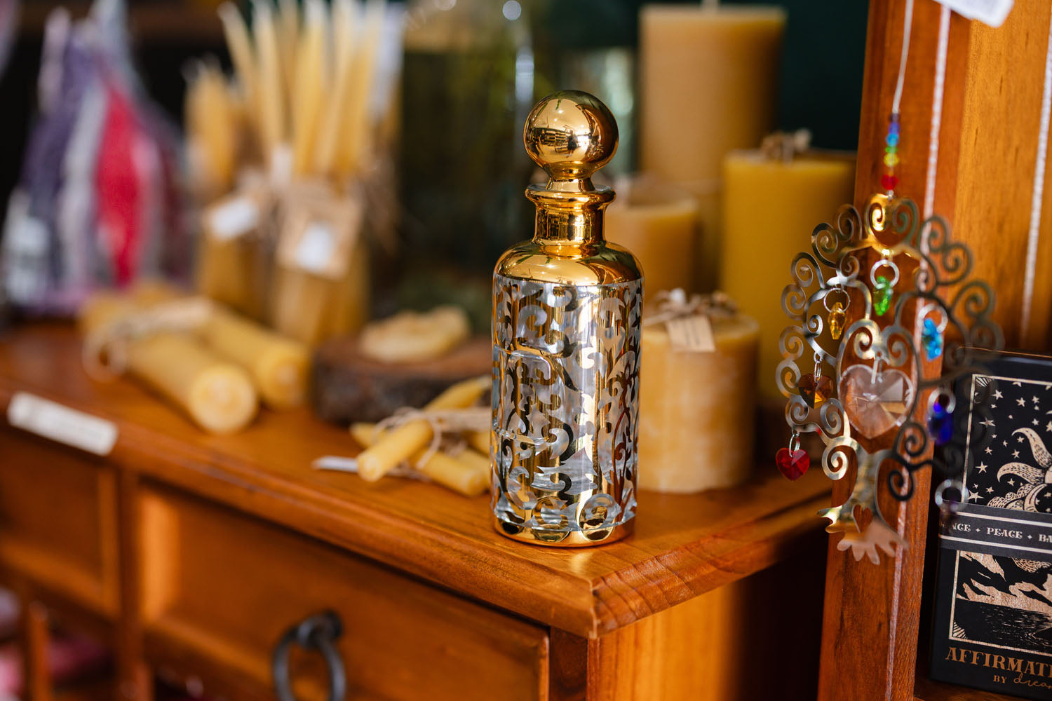 A chest of drawers topped with candles and a fancy gold bottle