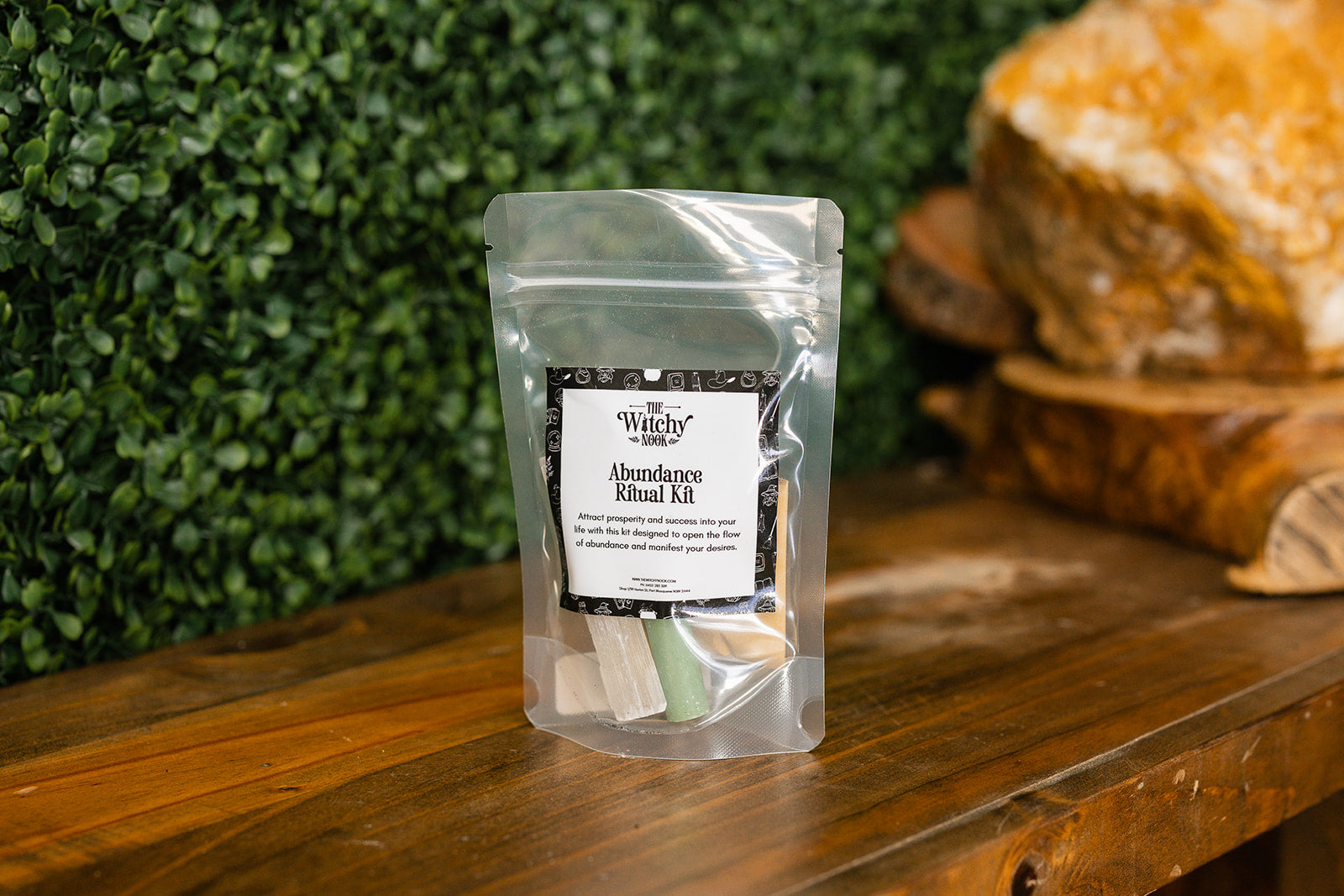 Packaged product labeled ‘Abundance Ritual Kit' by 'Witchy Nook' on a wooden surface with greenery in the background.