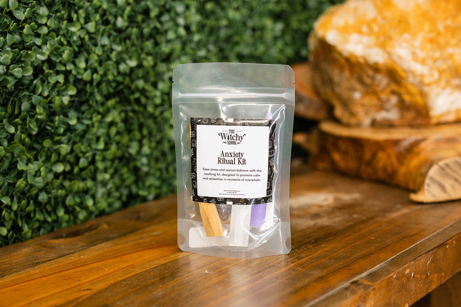 Packaged product labeled ‘Anxiety Ritual Kit' by 'Witchy Nook' on a wooden surface with greenery in the background.