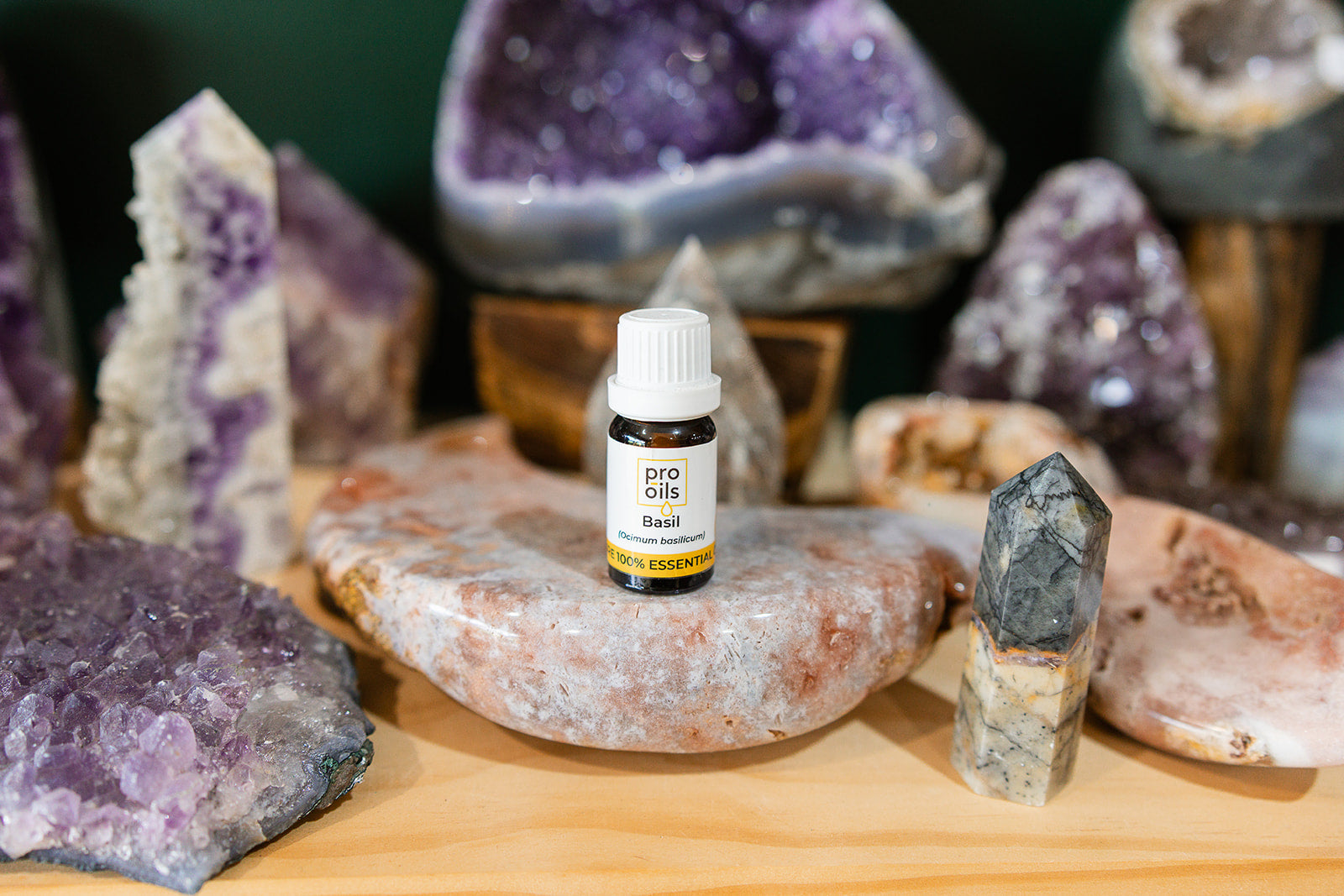 Small bottle of Basil Essential Oil on a wooden surface with crystals in the background