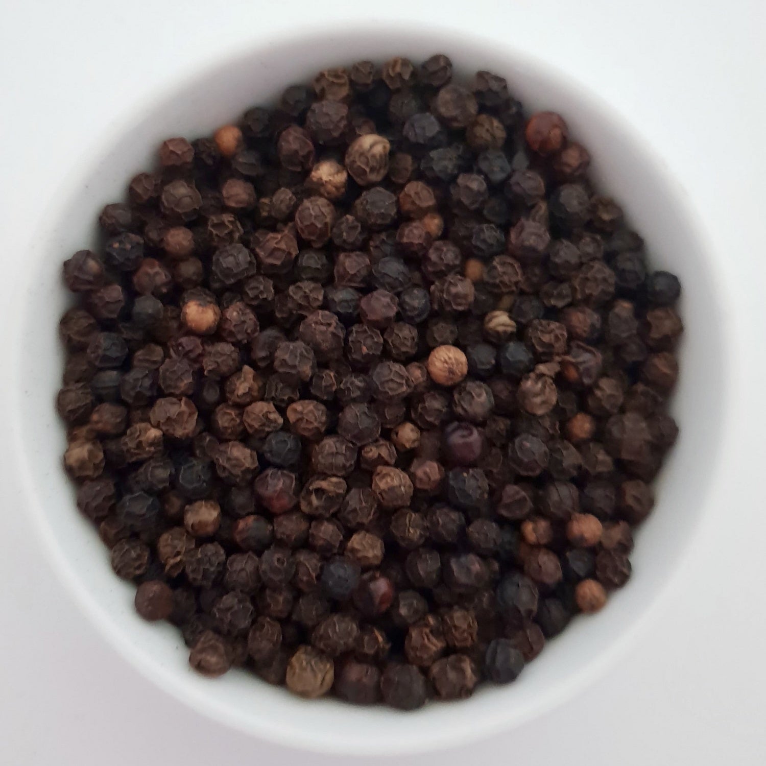 Black Peppercorns herb on a white surface.