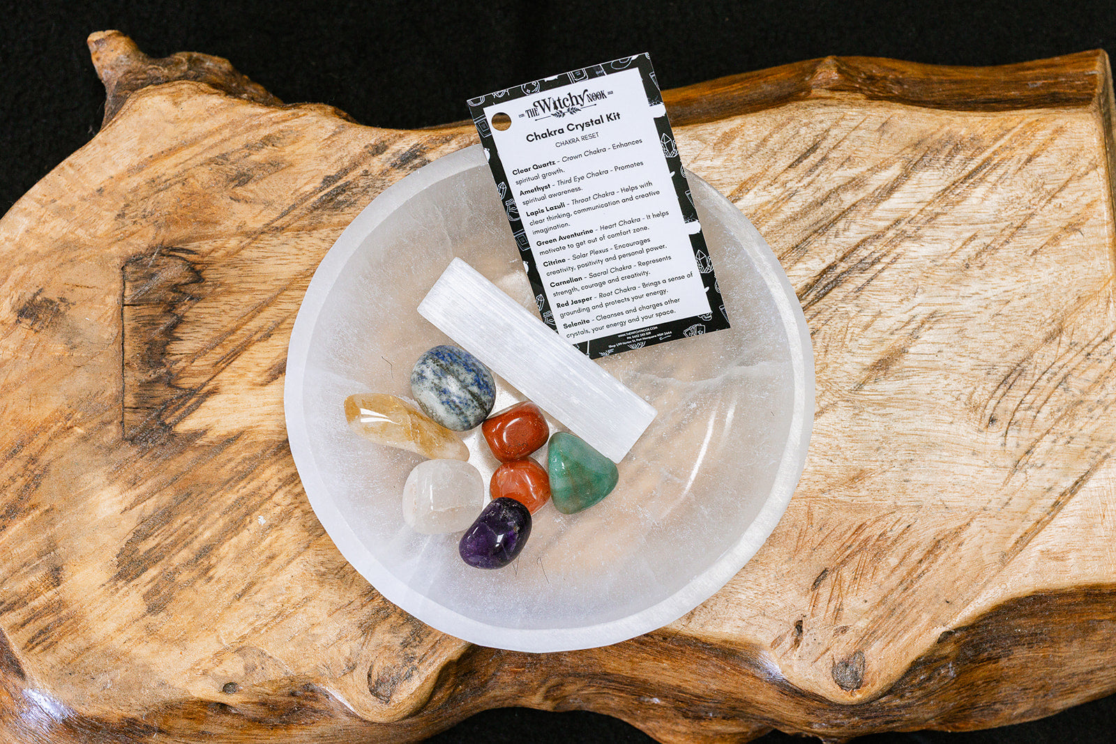 Packaged product labeled 'Chakra Essentials Tumble Kit' by 'Witchy Nook' on a wooden surface in the background with products displayed in a bowl.