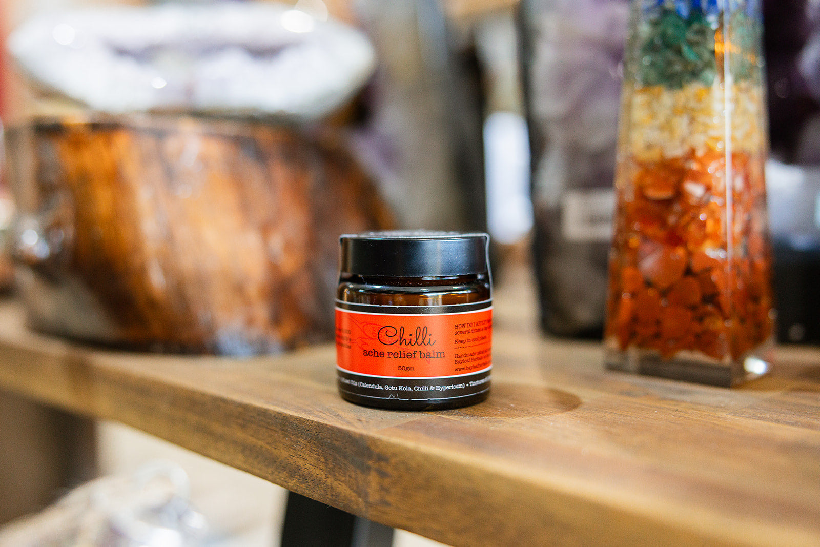 Balms and rubs Chili Ache Relief Balm displayed on a wooden surface with a blurred background