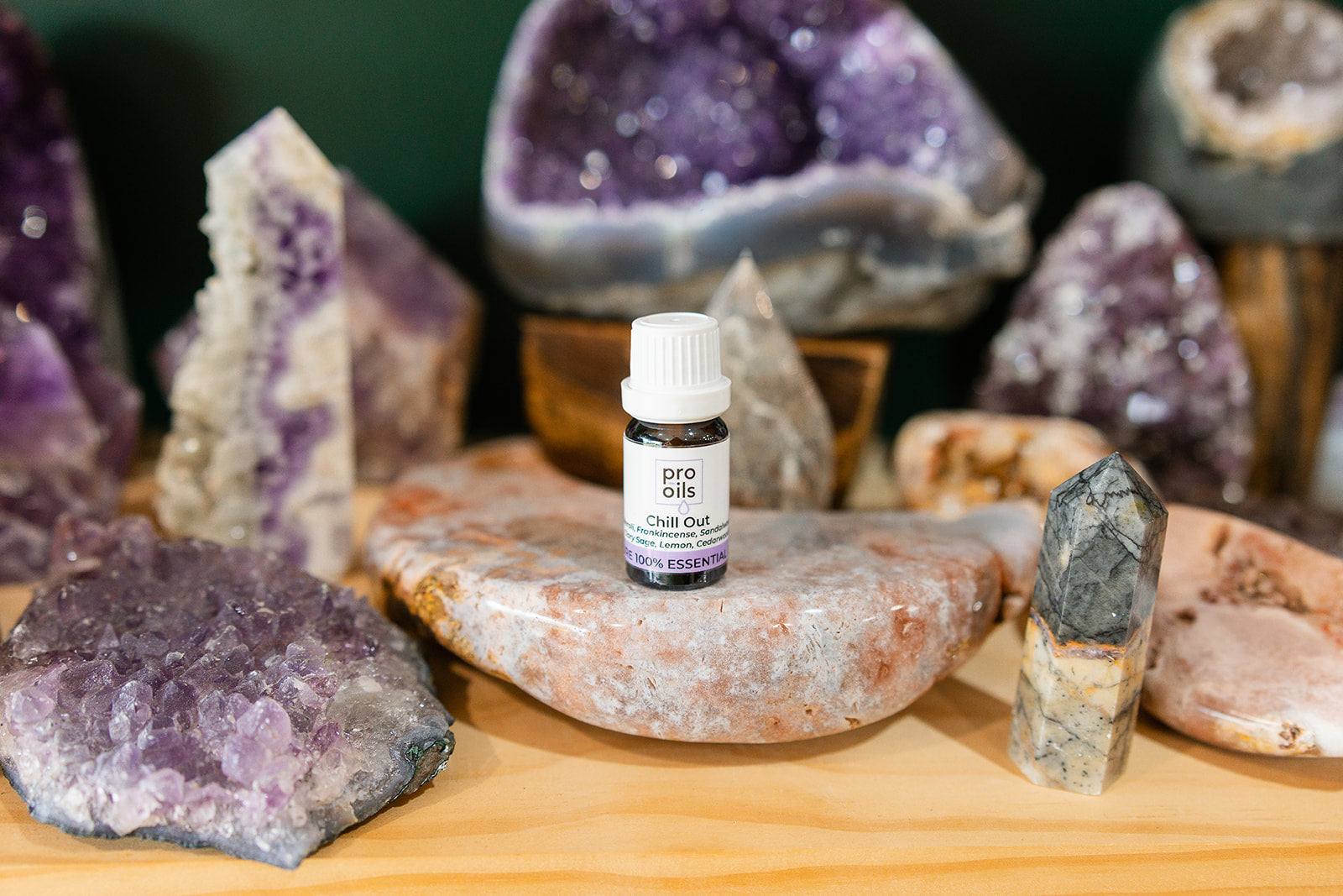 Small bottle of Chill Out Essential Oil Blend on a wooden surface with crystals in the background