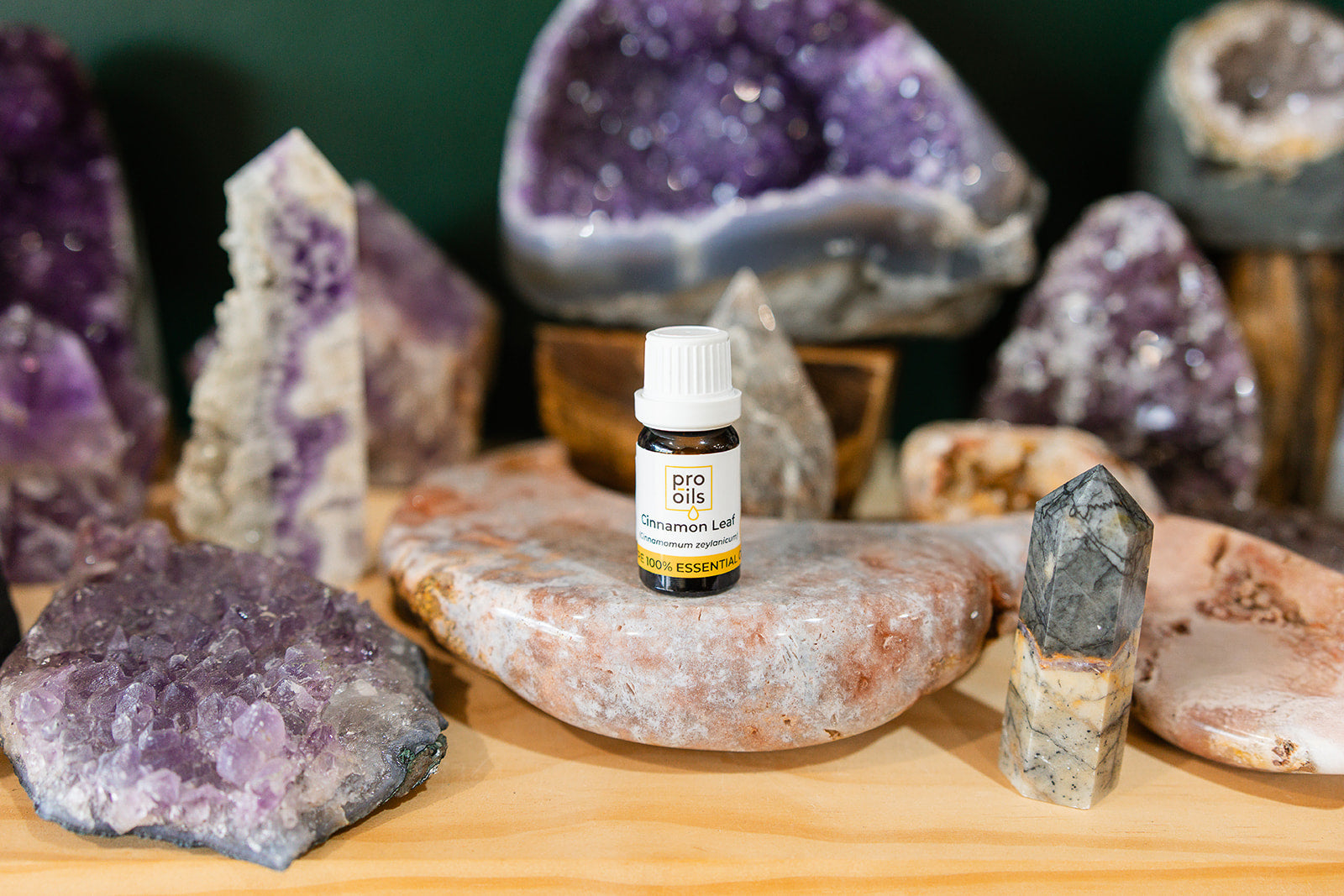 Small bottle of Cinnamon Leaf Essential Oil on a wooden surface with crystals in the background