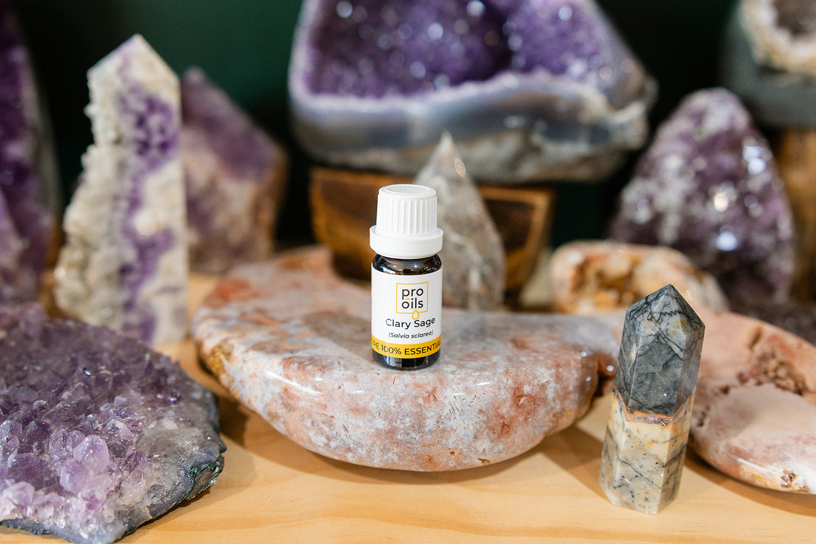 Small bottle of Clary Sage Essential Oil on a wooden surface with crystals in the background