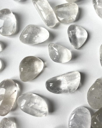 Displayed is a collection of Clear Quartz Tumbles also known as Rock crystals displayed on a white background