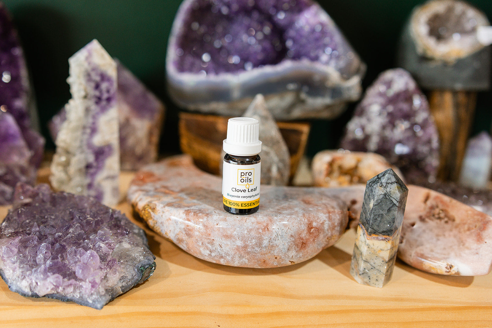 Small bottle of Clove Leaf Essential Oil on a wooden surface with crystals in the background