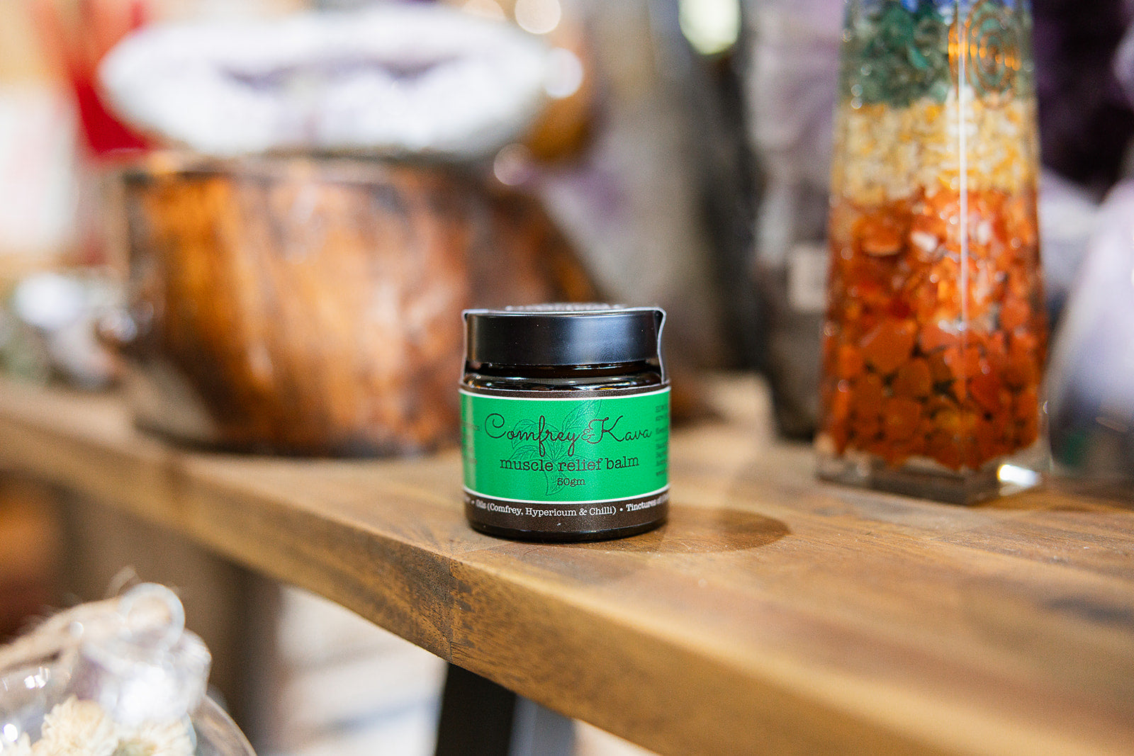 Balms and rubs Comfrey Kave Muscle Relief displayed on a wooden surface with a blurred background