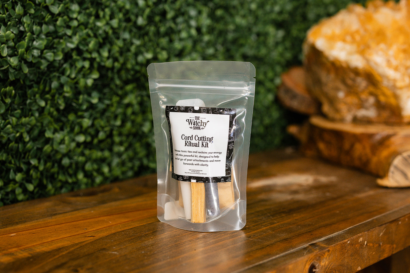Packaged product labeled 'Cord Cutting Ritual Kit' by 'Witchy Nook' on a wooden surface with greenery in the background.
