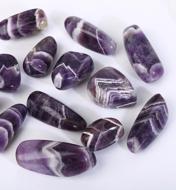 A collection of polished, tumbled stones known several names such as: Dream Amethyst or Chevron Amethyst or Banded Amethyst, displayed on a white background