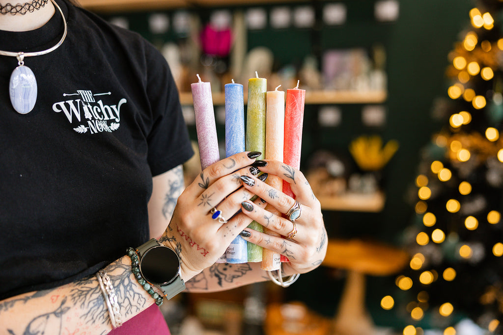Drippy Candles held by a person with tattoos wearing a t-shirt with The Witchy Nook printed on the front. 