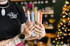 Drippy Candles held by a person with tattoos wearing a t-shirt with The Witchy Nook printed on the front. 