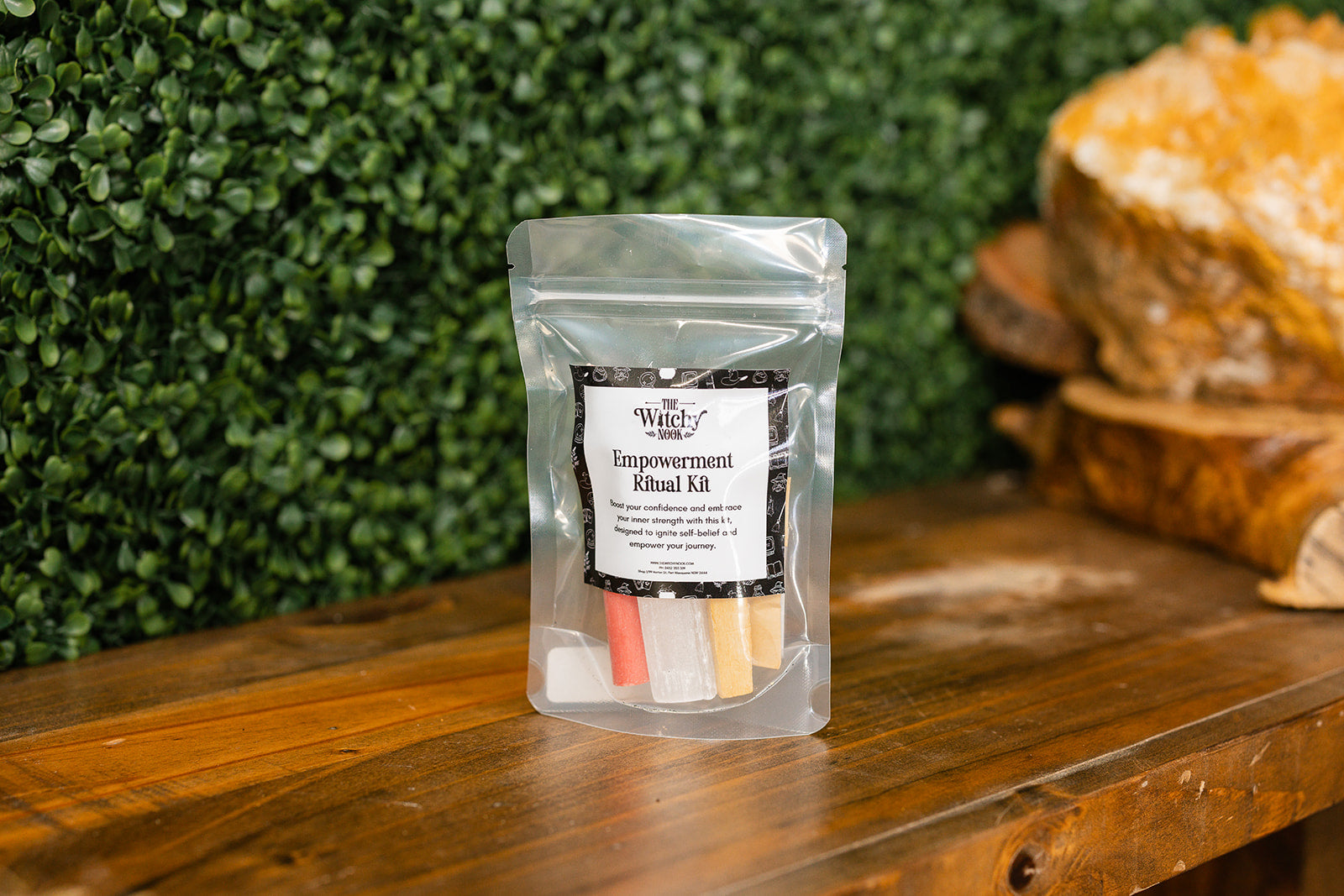 Packaged product labeled 'Empowerment Ritual Kit' by 'Witchy Nook' on a wooden surface with greenery in the background.