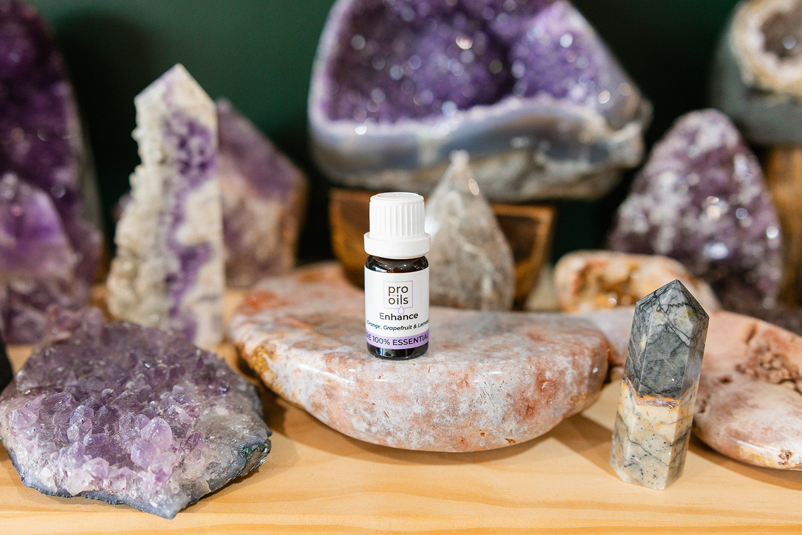 Small bottle of Enhance Essential Oil Blend on a wooden surface with crystals in the background