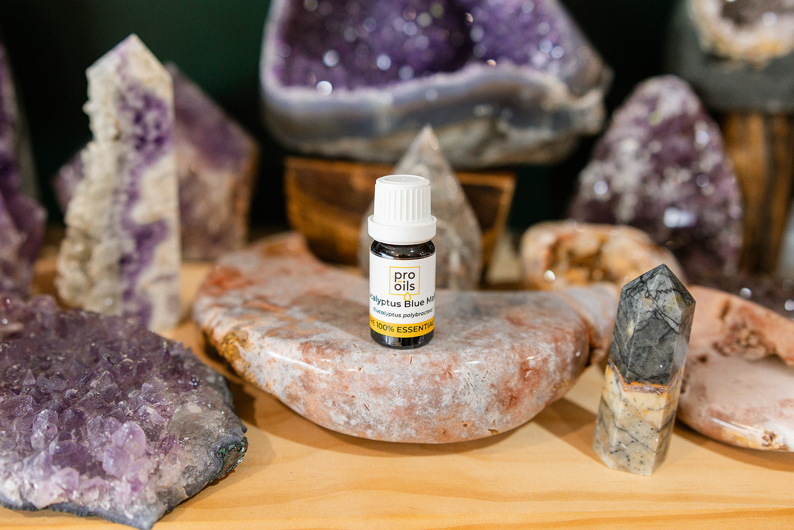 Small bottle of Eucalyptus Blue Mallee Essential Oil on a wooden surface with crystals in the background