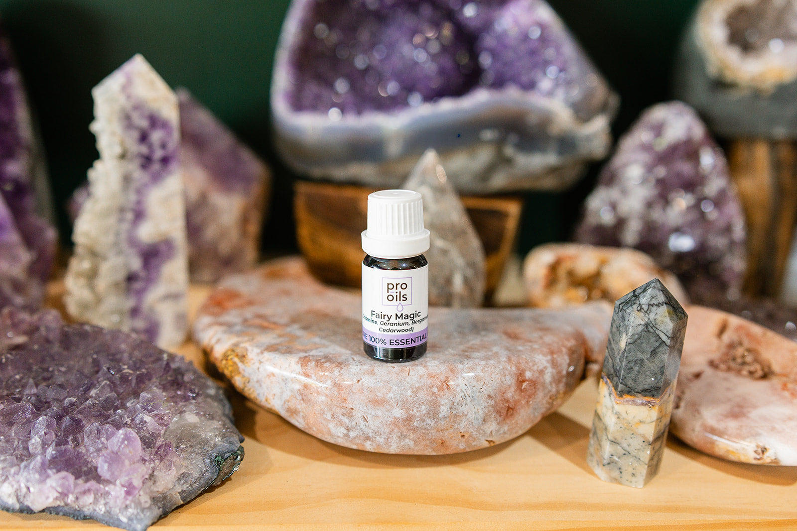 Small bottle of Fairy Magic Essential Oil Blend on a wooden surface with crystals in the background