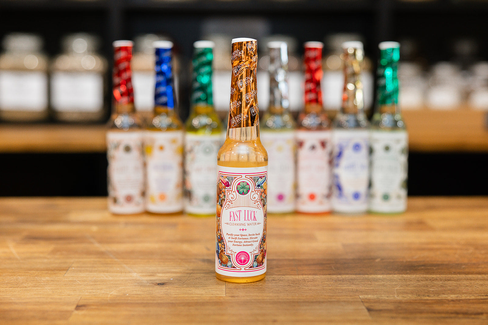 Bottle of Fast Luck Cleansing Water displayed in front of a collection of cleansing waters on a wooden background