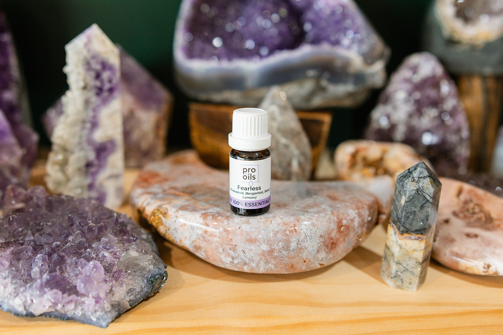Small bottle of Fearless Essential Oil Blend on a wooden surface with crystals in the background