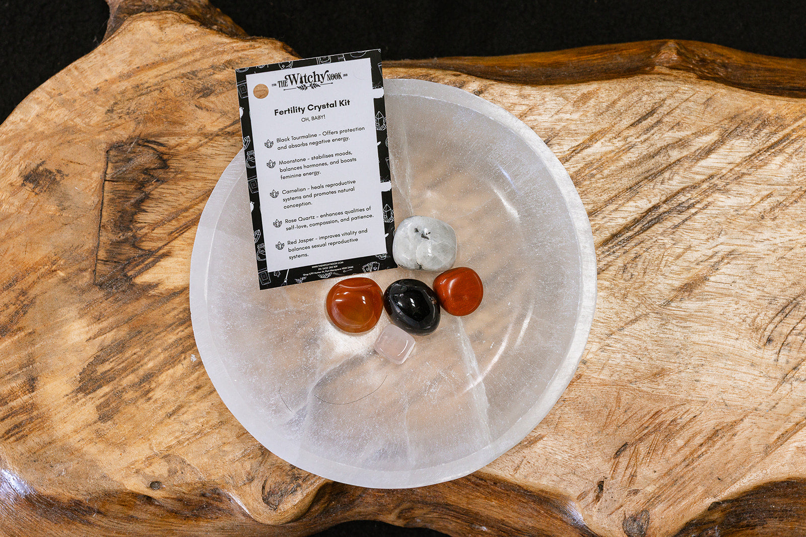 Packaged product labeled 'Fertility Tumble Kit' by 'Witchy Nook' on a wooden surface in the background with products displayed in a bowl.