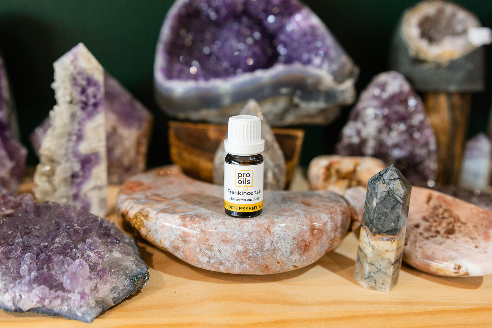 Small bottle of Frankincense Essential Oil on a wooden surface with crystals in the background
