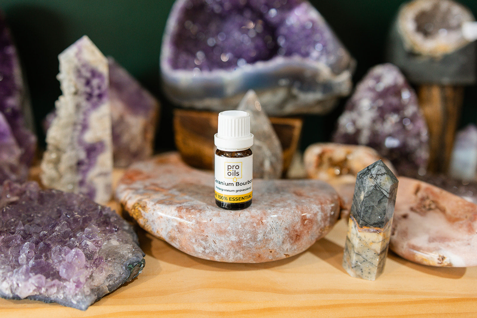 Small bottle of Geranium Bourbon Essential Oil on a wooden surface with crystals in the background