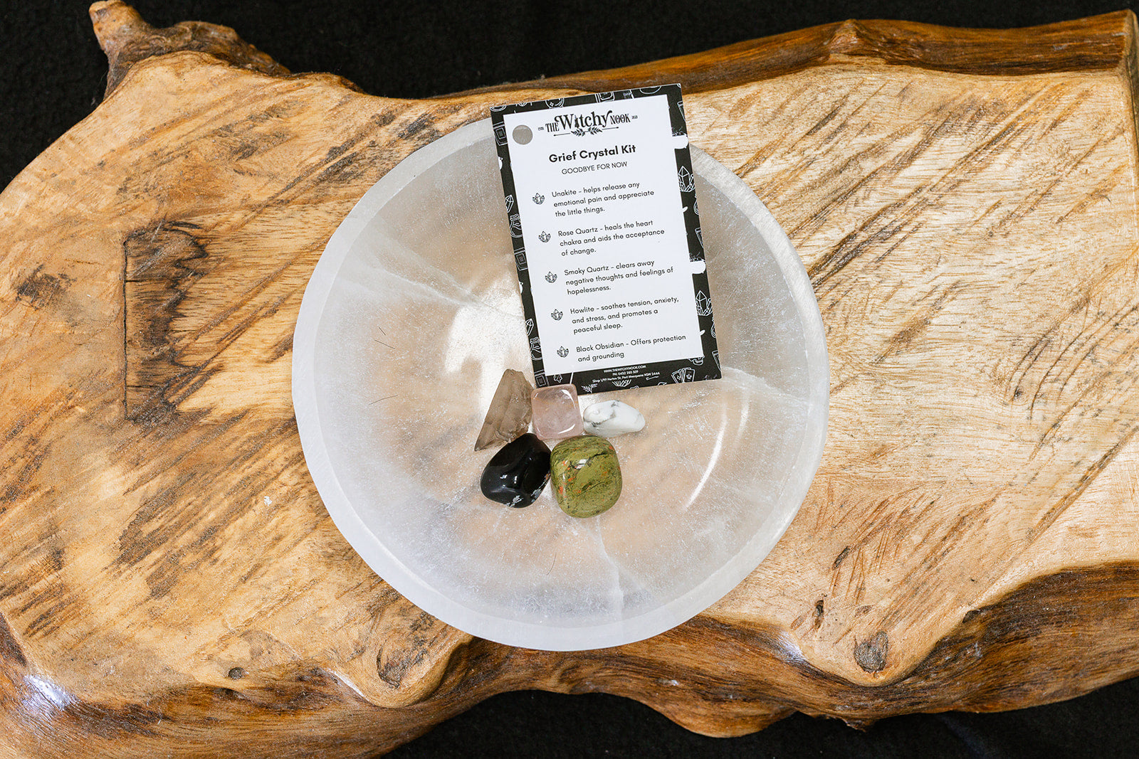 Packaged product labeled 'Grief Tumble Kit' by 'Witchy Nook' on a wooden surface in the background with products displayed in a bowl.