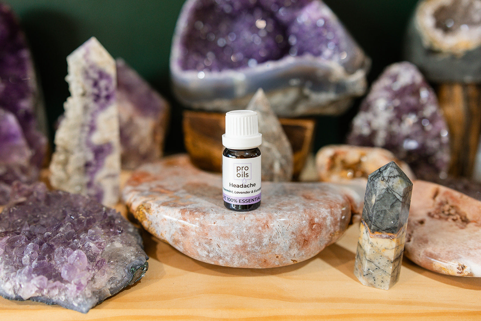 Small bottle of Headache Essential Oil Blend on a wooden surface with crystals in the background