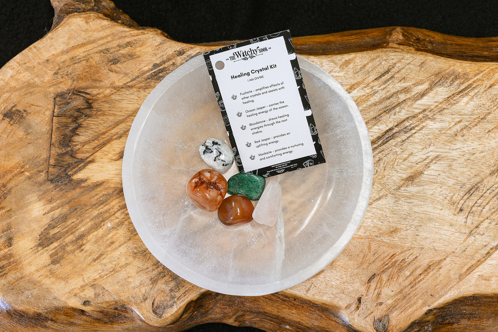 Packaged product labeled 'Healing Tumble Kit' by 'Witchy Nook' on a wooden surface in the background with products displayed in a bowl.