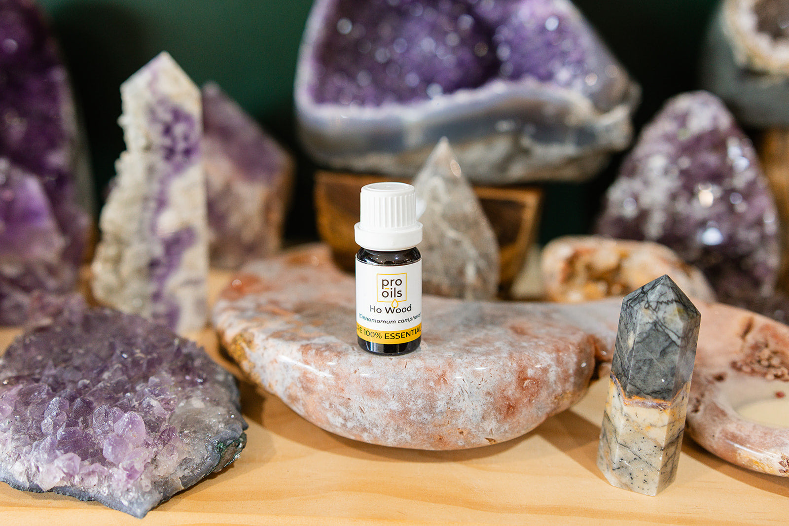 Small bottle of Ho Wood Essential Oil on a wooden surface with crystals in the background