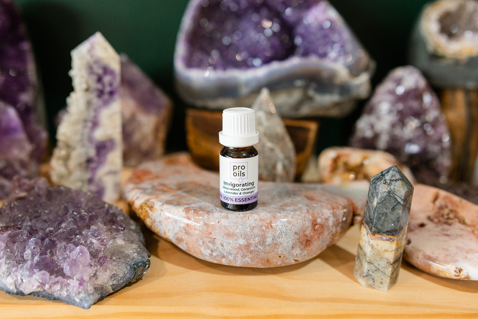 Small bottle of Invigorating Essential Oil Blend on a wooden surface with crystals in the background