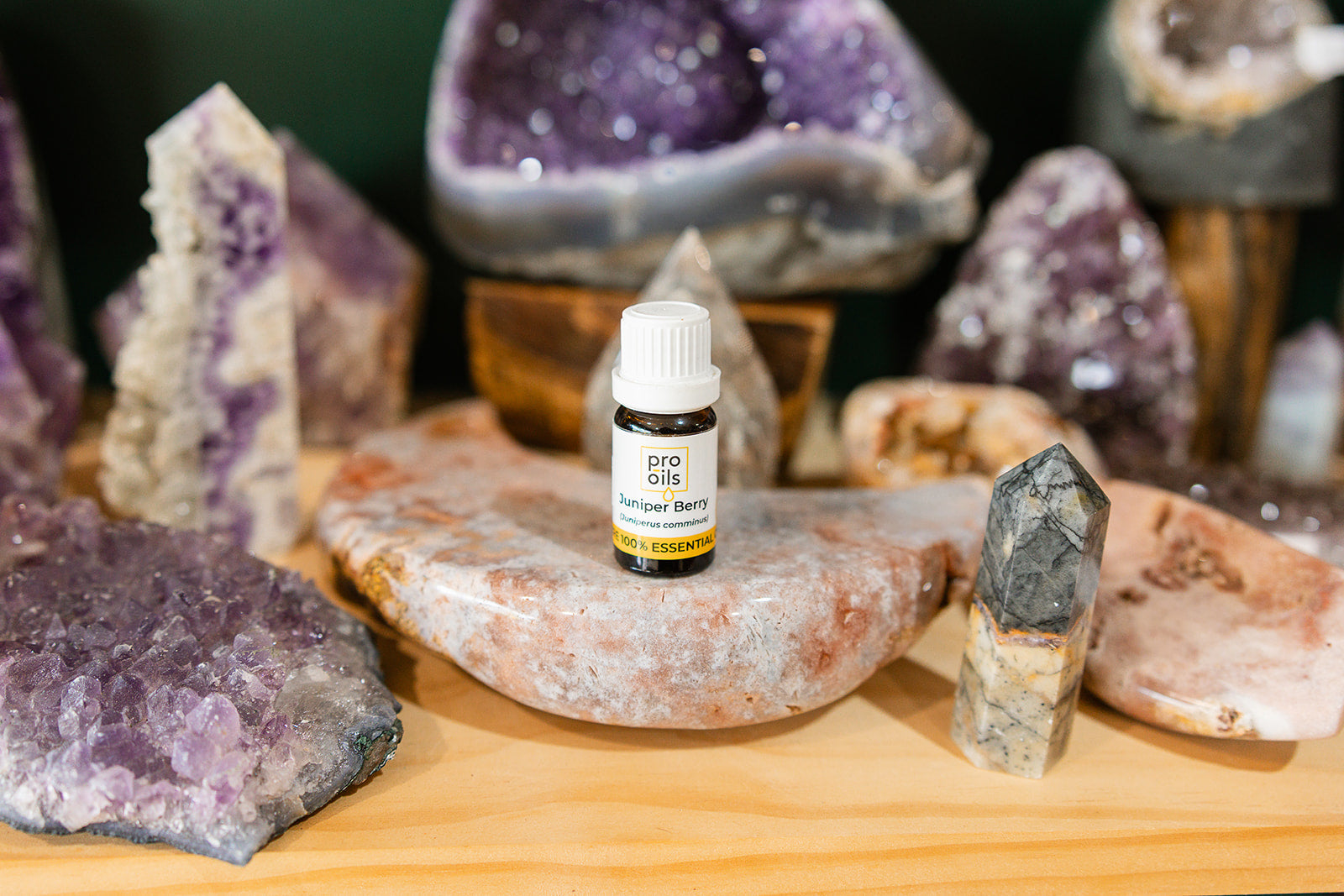 Small bottle of Juniper Berry Essential Oil on a wooden surface with crystals in the background
