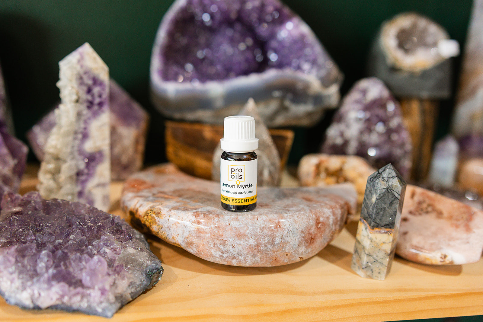 Small bottle of Lemon Myrtle Essential Oil on a wooden surface with crystals in the background