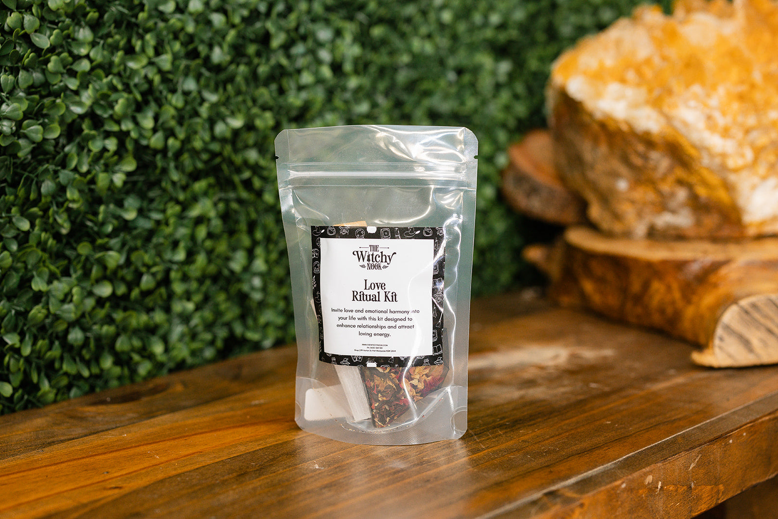 Packaged product labeled 'Love Ritual Kit' by 'Witchy Nook' on a wooden surface with greenery in the background.
