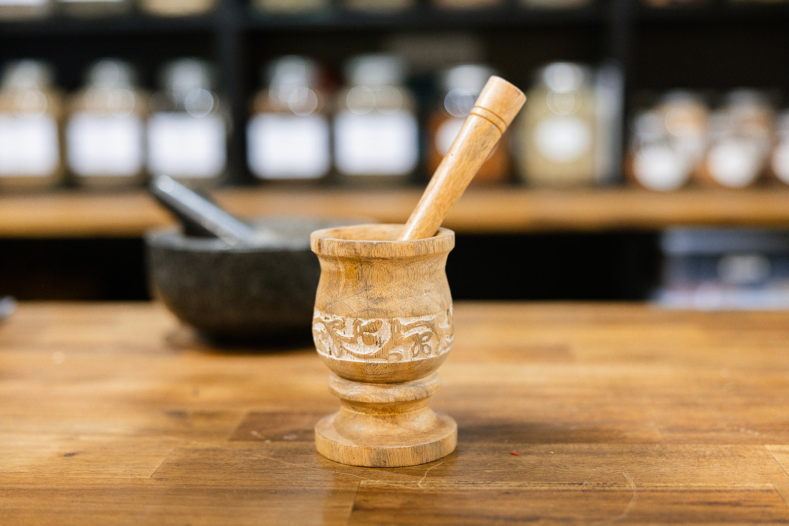 Wooden Mortar and pestle hand carved mango wood with a floral design displayed on a wooden bench with a blurred background.