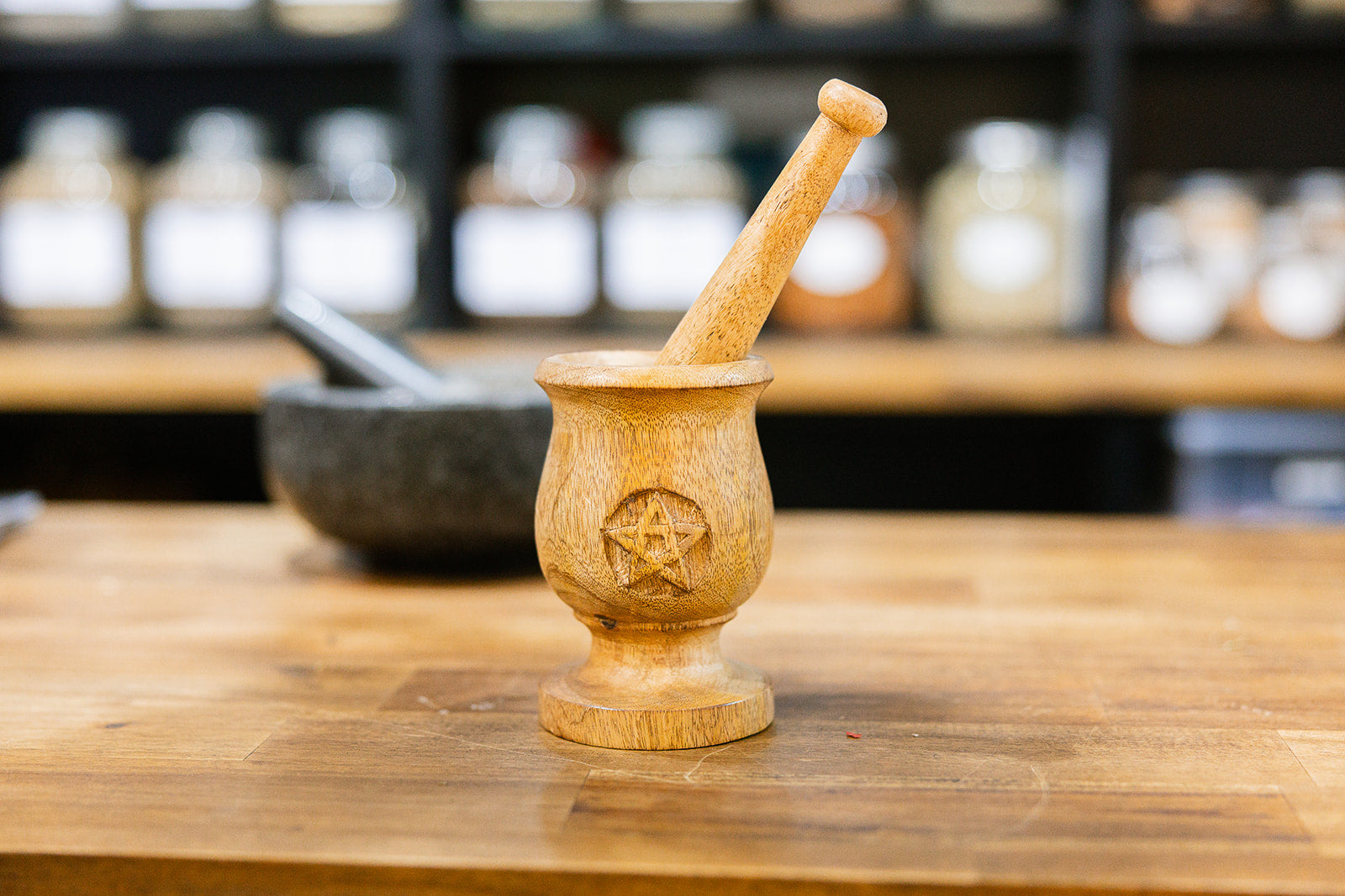 Wooden Mortar and pestle hand carved mango wood with a pentagram design displayed on a wooden bench with a blurred background.