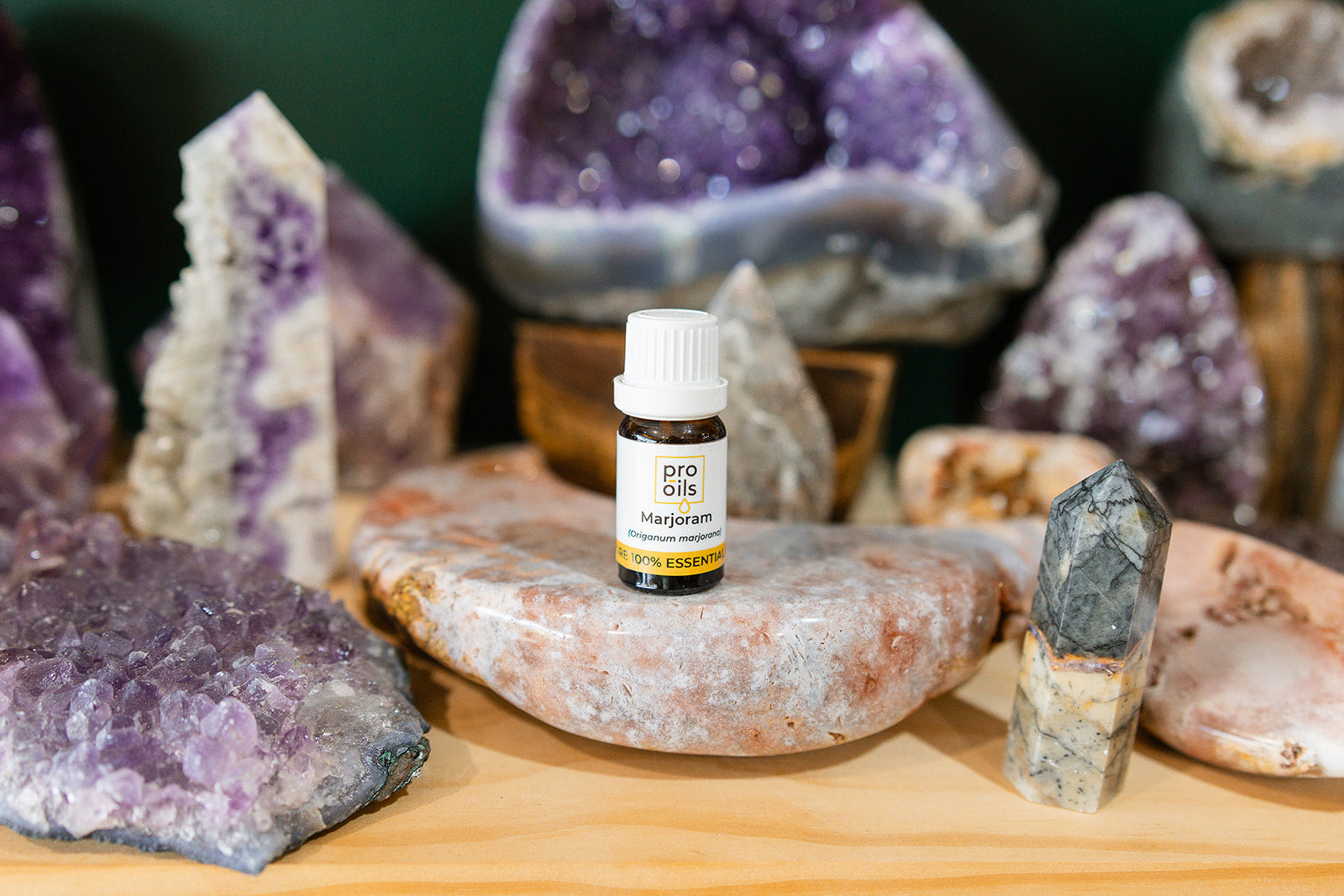 Small bottle of Marjoram Essential Oil on a wooden surface with crystals in the background