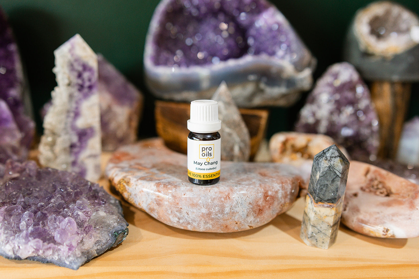 Small bottle of May Chang Essential Oil Blend on a wooden surface with crystals in the background
