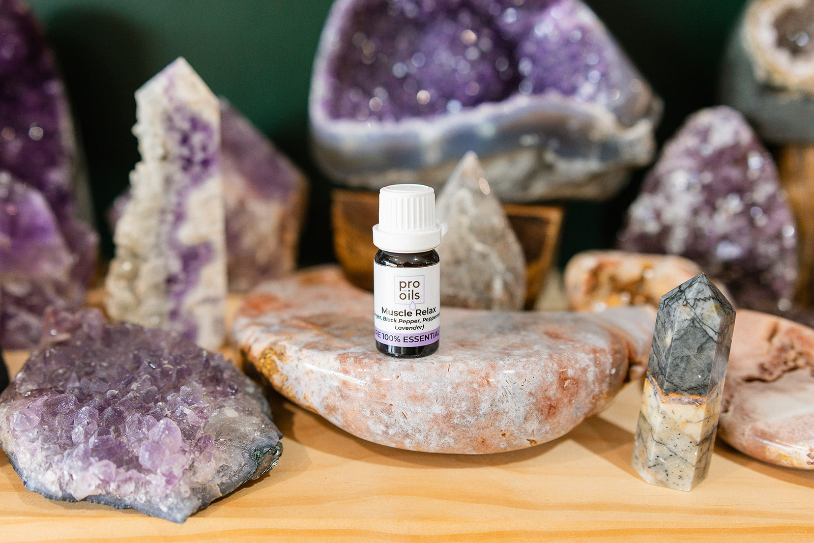 Small bottle of Muscle Relax Essential Oil Blend on a wooden surface with crystals in the background
