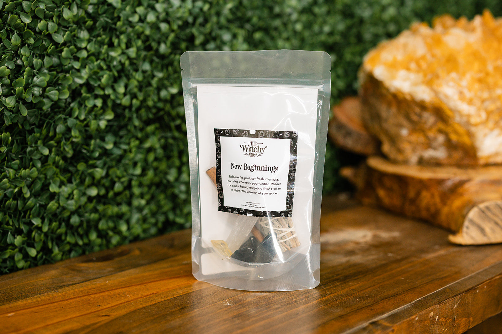Packaged product labeled 'New Beginnings Ritual Kit' by 'Witchy Nook' on a wooden surface with greenery in the background.