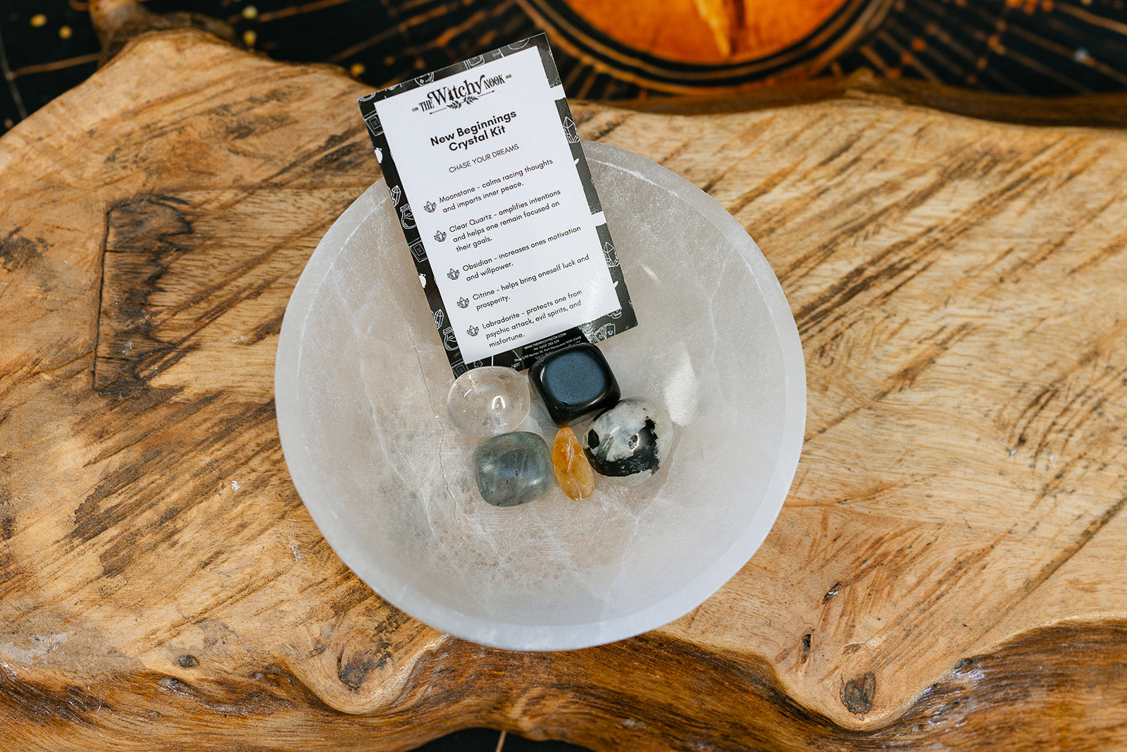 Packaged product labeled 'New Beginnings Tumble Kit' by 'Witchy Nook' on a wooden surface in the background with products displayed in a bowl.