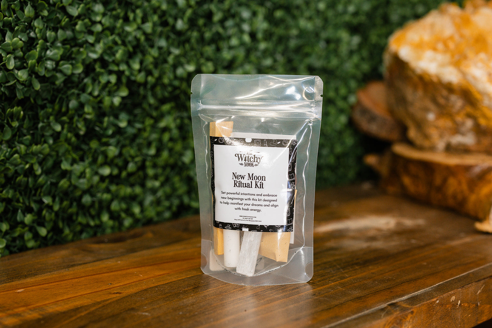 Packaged product labeled 'New Moon Ritual Kit' by 'Witchy Nook' on a wooden surface with greenery in the background.
