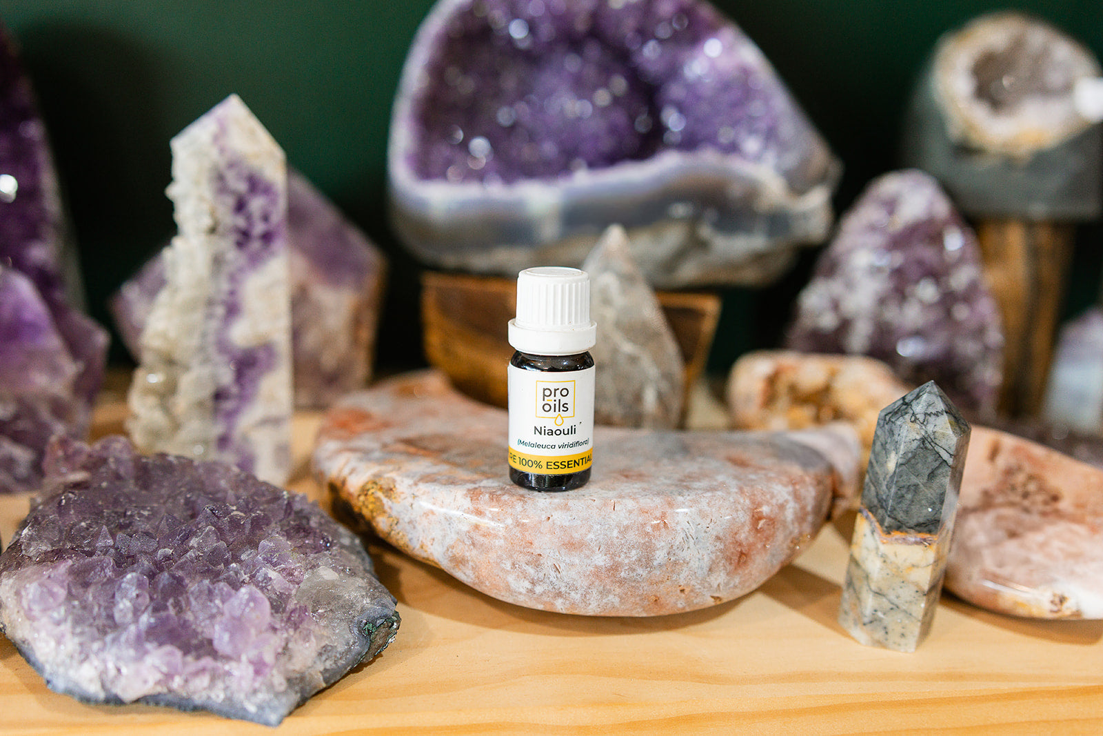 Small bottle of Niaouli Essential Oil on a wooden surface with crystals in the background