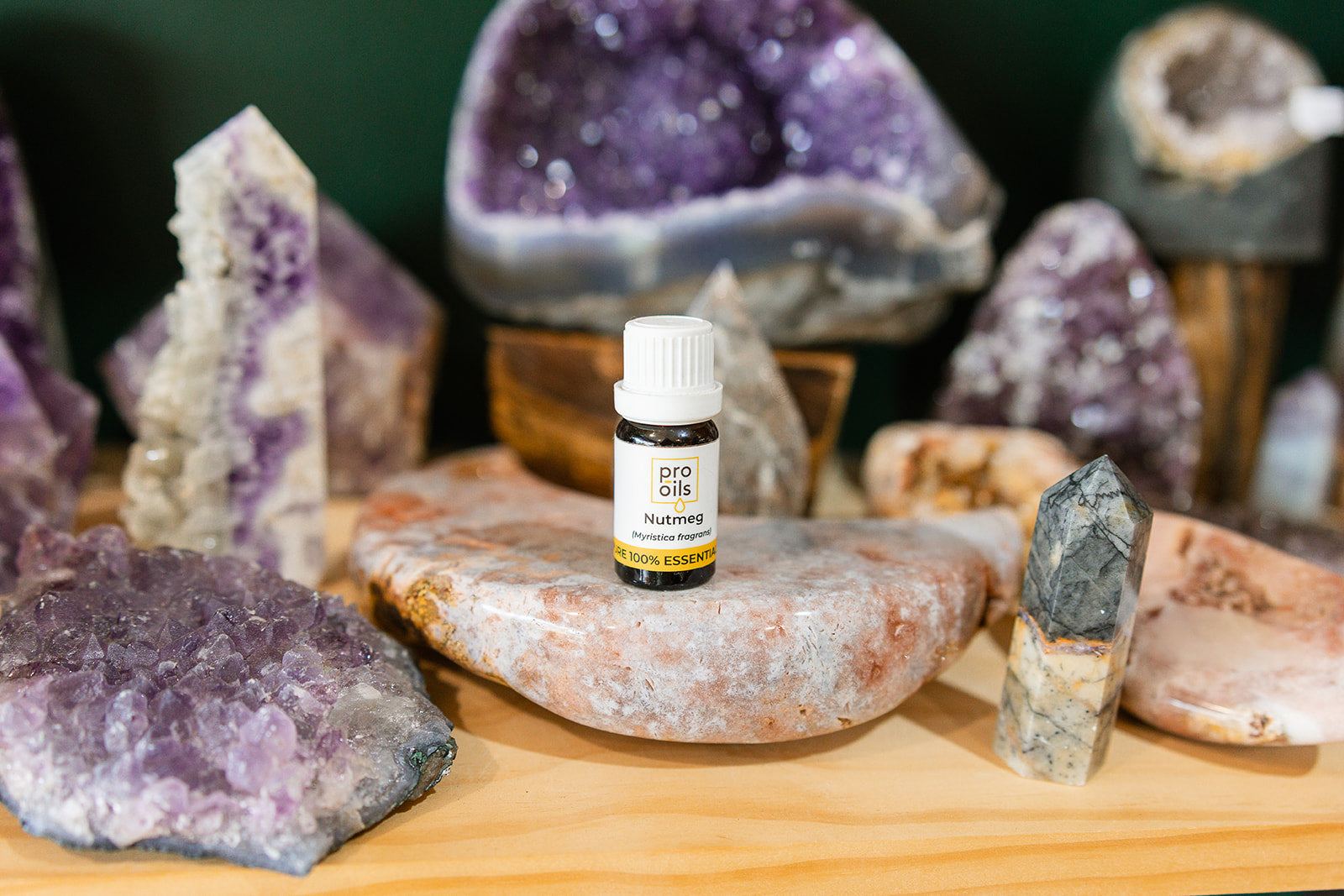 Small bottle of Nutmeg Essential Oil on a wooden surface with crystals in the background
