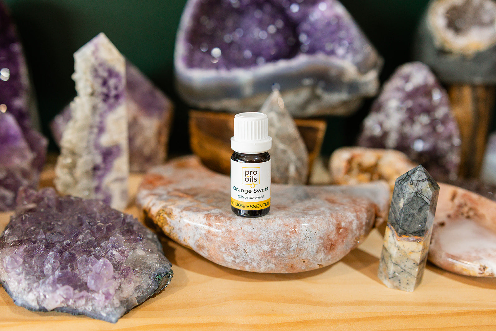 Small bottle of Orange Sweet Essential Oil on a wooden surface with crystals in the background