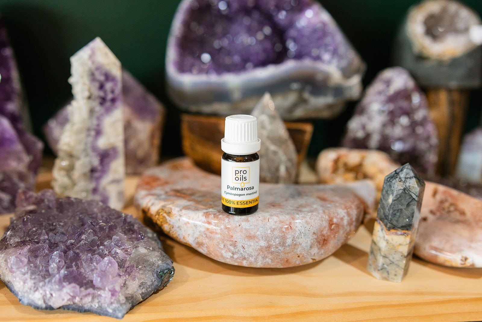 Small bottle of Palmarosa Essential Oil on a wooden surface with crystals in the background