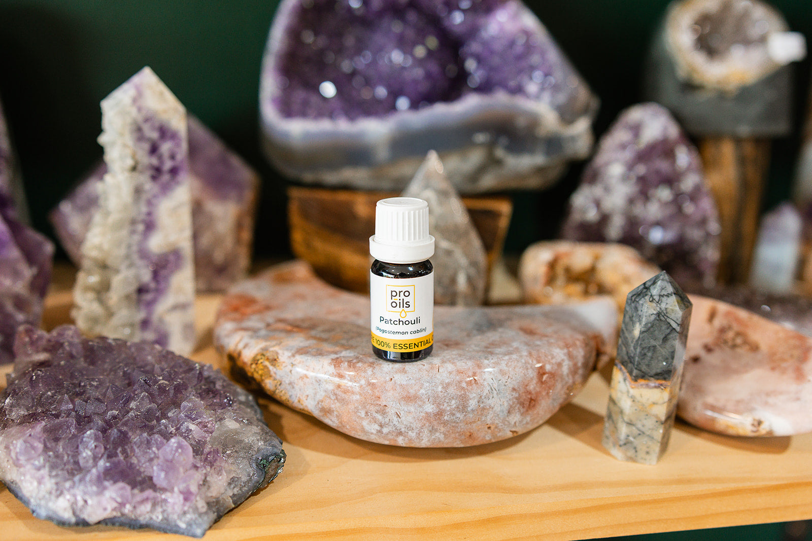 Small bottle of Patchouli Essential Oil on a wooden surface with crystals in the background