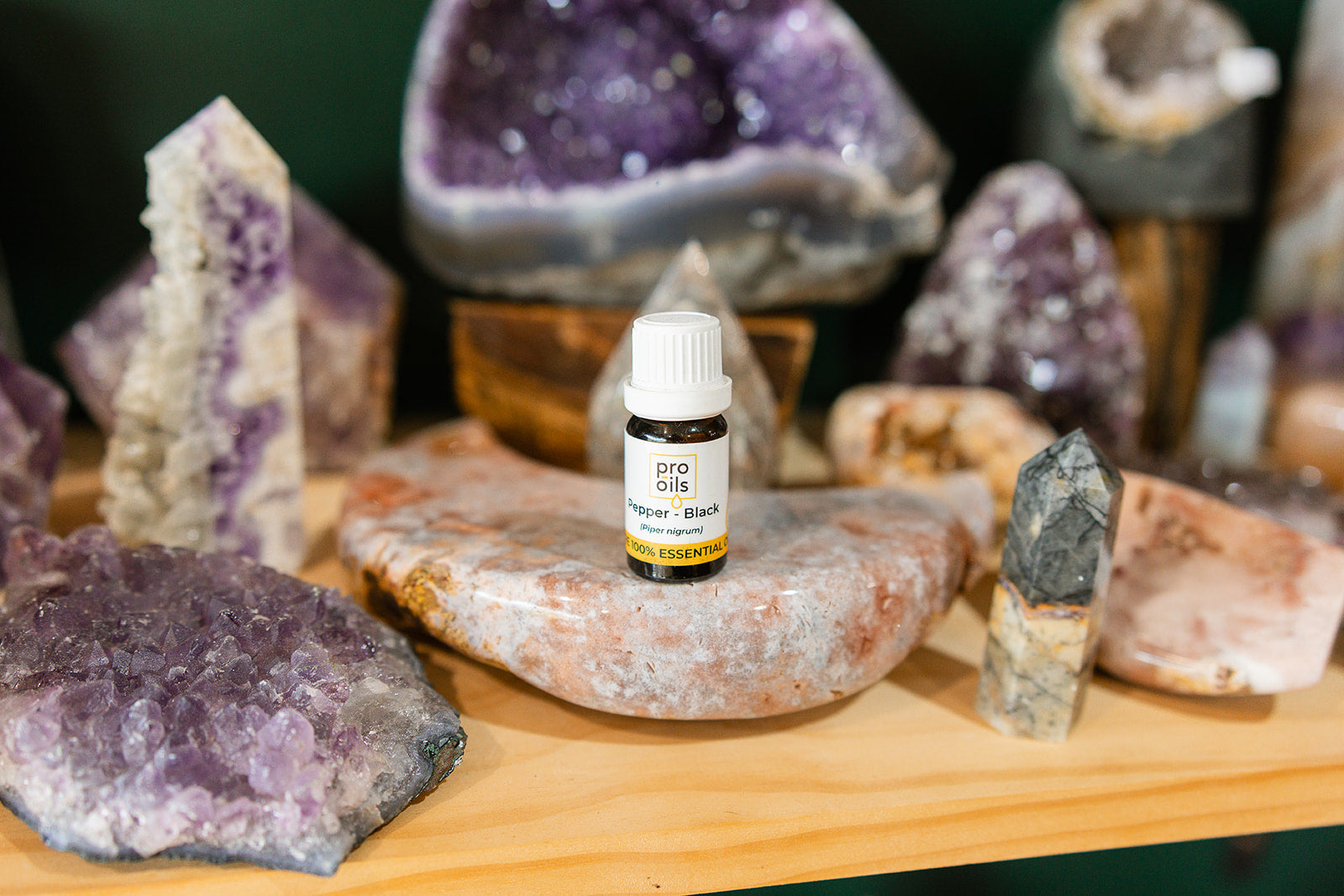 Small bottle of Pepper Black Essential Oil on a wooden surface with crystals in the background